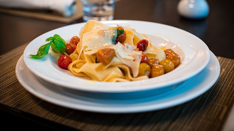 Delicious pasta with cherry tomatoes topped with thin-sliced cheese and herbs.